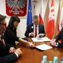 Powiększ zdjęcie Przy stole od prawej siedzą: Wicestarosta Włoszczowski Łukasz Karpiński, Wojewoda Świętokrzyski Zbigniew Koniusz podpisuje druk umowy, Skarbnik Powiatu Agnieszka Górska sięga reką po druk na stole, Starosta Włoszczowski Dariusz Czechowski. 