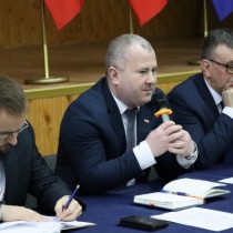 Powiększ zdjęcie Za stołem nakrytym granatowym obrusem od lewej siedzą Rafał Pacanowski – członek  Zarządu Powiatu Włoszczowskiego, z mikrofonem w ręce wicestarosta włoszczowski Łukasz Karpiński, starosta dariusz Czechowski.