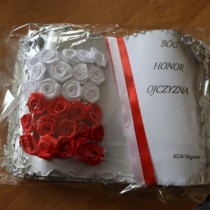 Powiększ zdjęcie Laurka w kształcie księgi wykonana przez KGW Bieganów. Z lewej strony biało - czerwona flaga wykonana z kwiatów z bibuły, z prawej strony Biało czerwona szarfa i napis: BÓG, HONOR, OJCZYZNA i KGW Bieganów.