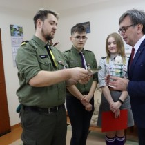 Powiększ zdjęcie Od prawej stoją: Starosta Włoszczowski Dariusz Czechowski, który trzyma w rękach lampion w kształcie zielonej choinki, harcerka i dwaj harcerze. Jeden z nich przekazuje Staroście kartkę z życzeniami. 