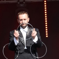 Powiększ zdjęcie Magik w czarnym fraku trzyma trzy metalowe kółka.