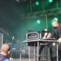 Powiększ zdjęcie Ubrany na czarno mężczyzna na scenie przesuwa skrzynię z której wystają ludzkie stopy.