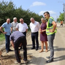 Powiększ zdjęcie Sprawdzanie warstwy podbudowy przez Inspektora Nadzoru. Wokół wykopu stoją przedstawiciele Powiatu, społeczności lokalnej i wykonawcy robót.