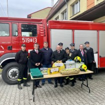 Powiększ zdjęcie Poseł Mariusz Gosek, Starosta Włoszczowski Dariusz Czechowski i Wójt Gminy Radków Jarosław Dominik ze strażakami z OSP Radków. Na stole leży nowy sprzęt i odzież