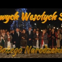 Powiększ zdjęcie Kadr z filmu promującego płytę. Przed Starostwem Powiatowym przy choince stoja uczestnicy nagrania. na obrazku żółty napis Wesołych Świąt Bożego Naropdzenia. W prawym górnym rogu napis Włoszczowa Online.