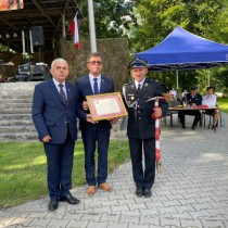 Powiększ zdjęcie Starosta Włoszczowski i Przewodniczący Rady Powiatu Włoszczowskiego wręczają strażakowi z OSP Secemin pamiątkowy grawerton i „HOOLIGAN”