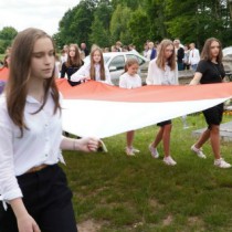Powiększ zdjęcie Przemarsz uczestników uroczystości. Dzieci niosą biało-czerwoną flagę